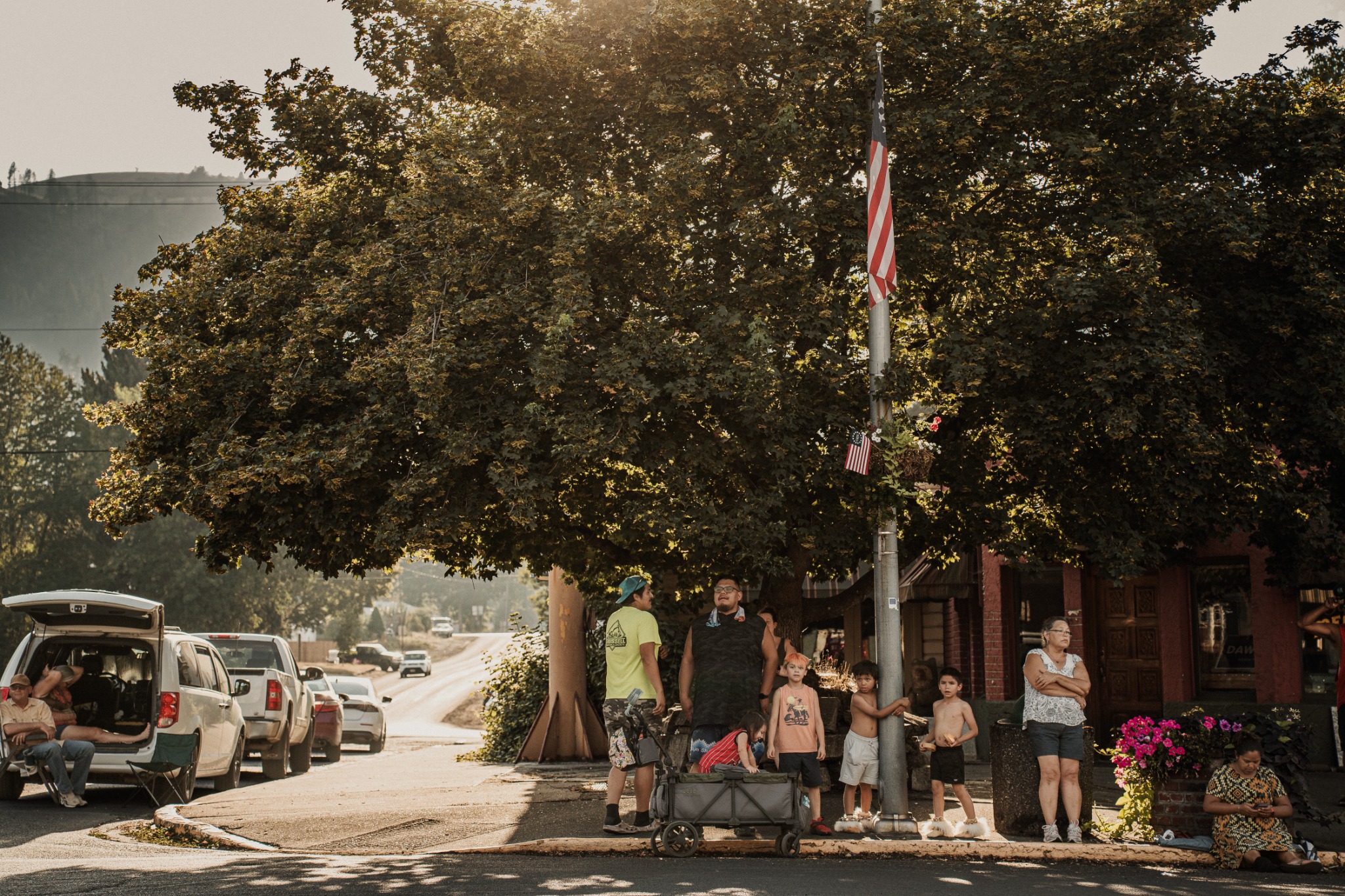 People gathered beneath a large tree on a Kamiah street